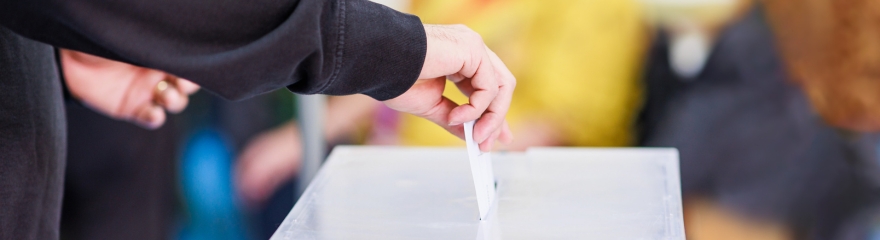 Close up of hand placing a voting card in a ballot box
